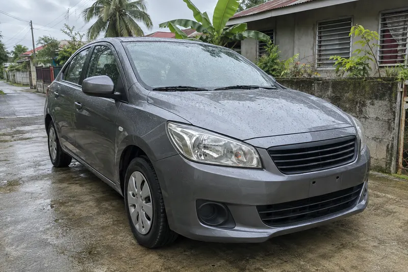 A small grey saloon washed and beaded with water on a driveway outside a house.