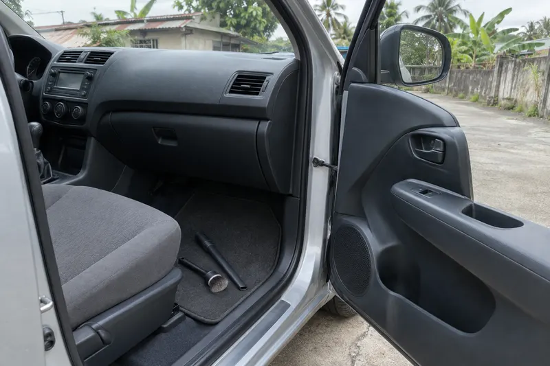 A vacuum nozzle and a soft detailing brush resting on the clean mat of a car footwell, the door open to a driveway.