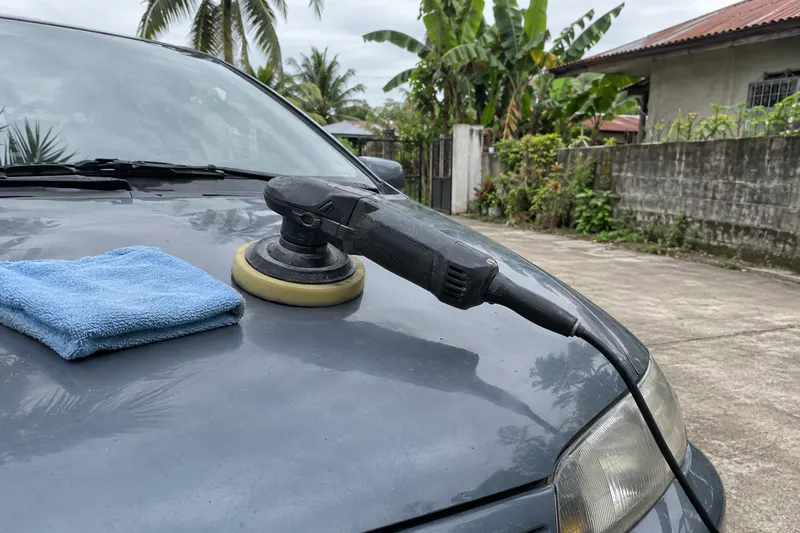 A polisher resting face down on a car bonnet with a folded microfibre cloth beside it.