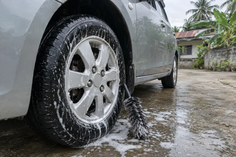 Suds running down an alloy wheel and tyre with a wheel brush leaning against it.